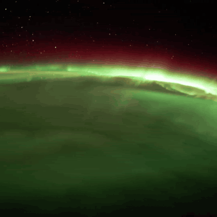 Green and red aurora glowing over the curve of the Earth at night, filmed from the International Space Station